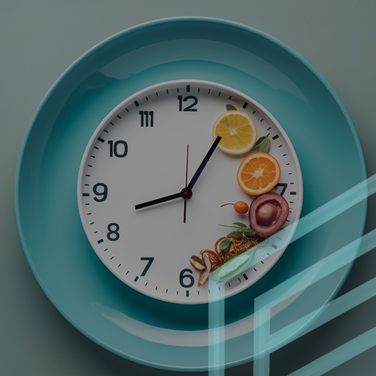 A round wall clock has mixed foods, including lemon slices, onions, and herbs, positioned around its edge. The clock is placed on a teal plate, and there is a transclucent geometric shape overlay partially covering the image from the right.