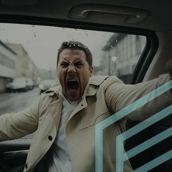 A man wearing a beige coat is sitting in a car with the door open, yelling angrily. It's raining outside and the car window has raindrops. The man appears frustrated or upset. There is a geometric pattern overlay on the right side of the image.