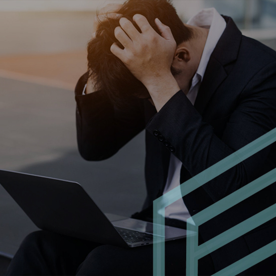 A man in a suit is sitting with his hands gripping his hair in frustration. An open laptop is on his lap. The background is blurred, suggesting an urban outdoor setting and there is a partially visible abstract graphic design overlay.