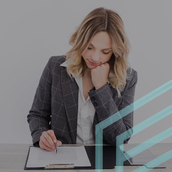 A woman with blonde hair wearing a gray checkered blazer is sitting at a table, focusing on documents in a black folder. She is holding a pen and has a thoughtful expression. Light blue geometric shapes are overlaid in the lower right corner of the image.