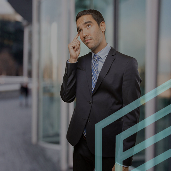 A man in a business suit stands pensively, touching his temple with his finger. He is outdoors in a modern urban setting with glass buildings in the background. He has an expression of deep thought or contemplation. A geometric design overlays part of the image.