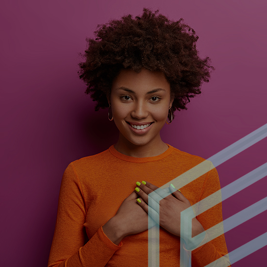 A woman with curly hair smiles while resting her hands on her chest. She is wearing an orange long-sleeve shirt and has bright green nail polish. The background is a solid maroon color with a semi-transparent abstract geometric overlay.