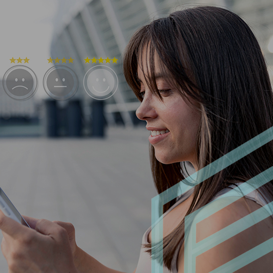 A woman with long brown hair is looking at her phone and smiling. She is standing outdoors near a building with a curved glass structure. Above her head are three rating emojis: a sad face, a neutral face, and a happy face with yellow stars.