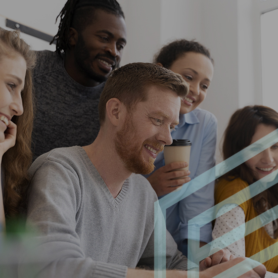 A diverse group of five people are gathered closely together, smiling and engaged while looking at a laptop screen. One person is holding a coffee cup. The atmosphere appears collaborative and friendly.