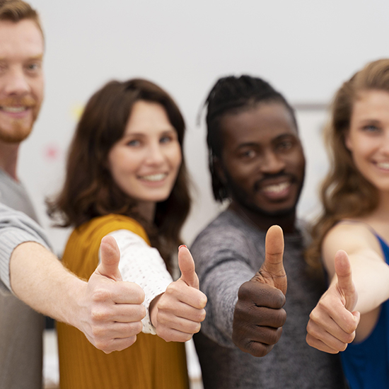 Four people are standing in a row, smiling and giving thumbs up towards the camera. They are dressed casually and appear to be in a positive and cheerful mood.