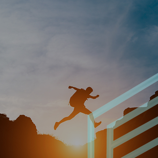 A silhouette of a person jumping between two cliff edges at sunset. The sky is filled with wispy clouds and has a warm golden hue. The person appears to be wearing a backpack. A set of parallel horizontal lines intersects the image near the bottom right corner.