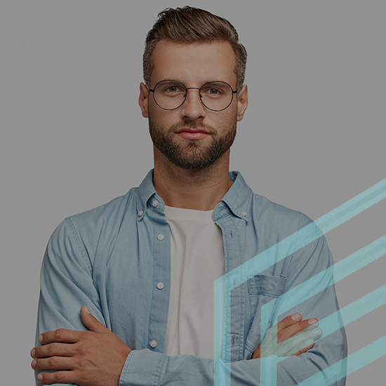 A man with short brown hair and a beard is wearing round glasses, a light blue button-up shirt over a white t-shirt, with his arms crossed. He stands against a plain gray background with transparent geometric shapes overlaid on the right side.