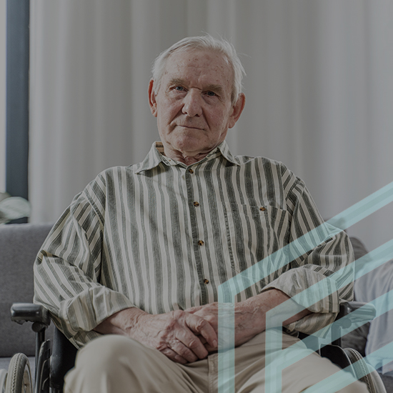 An elderly man with white hair sits in a wheelchair, resting his hands on his lap. He wears a striped shirt and beige pants. The background features light-colored curtains, giving the scene a calm and serene atmosphere.