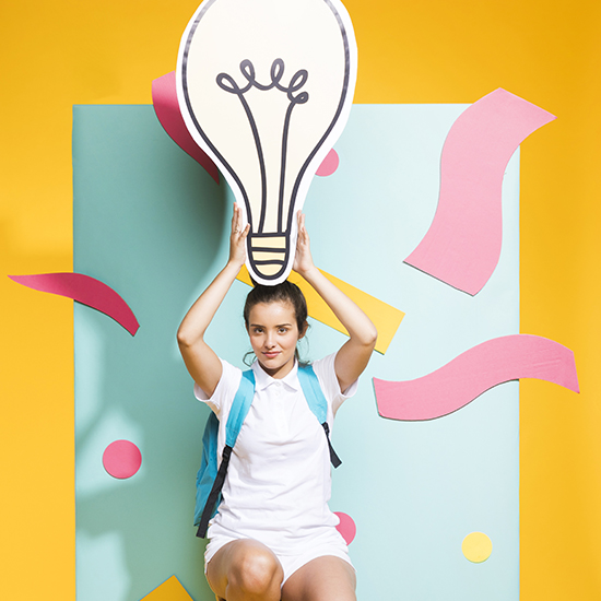 A person dressed in a white outfit and a backpack holds up a large, stylized paper cutout of a light bulb above their head. The background features a colorful and abstract arrangement of teal, pink, and yellow paper cutouts against a bright yellow backdrop.