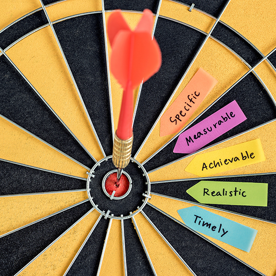 A dart hits the bullseye of a dartboard surrounded by vibrant sticky notes labeled "Specific," "Measurable," "Achievable," "Realistic," and "Timely," embodying the SMART goals framework—a key tool in self-improvement and effective goal setting.