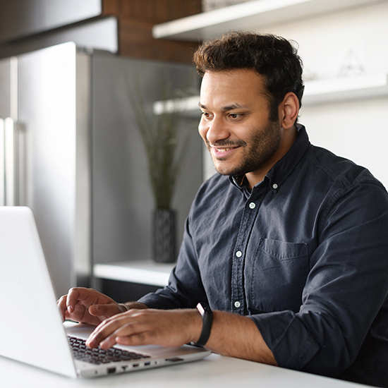 Smiling young indian guy using a laptop for remote work from home
