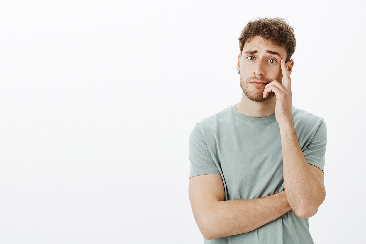unimpressed careless attractive young male with short fair hair, holding hand on cheek and staring with no care at camera, hearing stupid ideas during interview, standing uninterested over grey wall anxiety relief starts with control 2